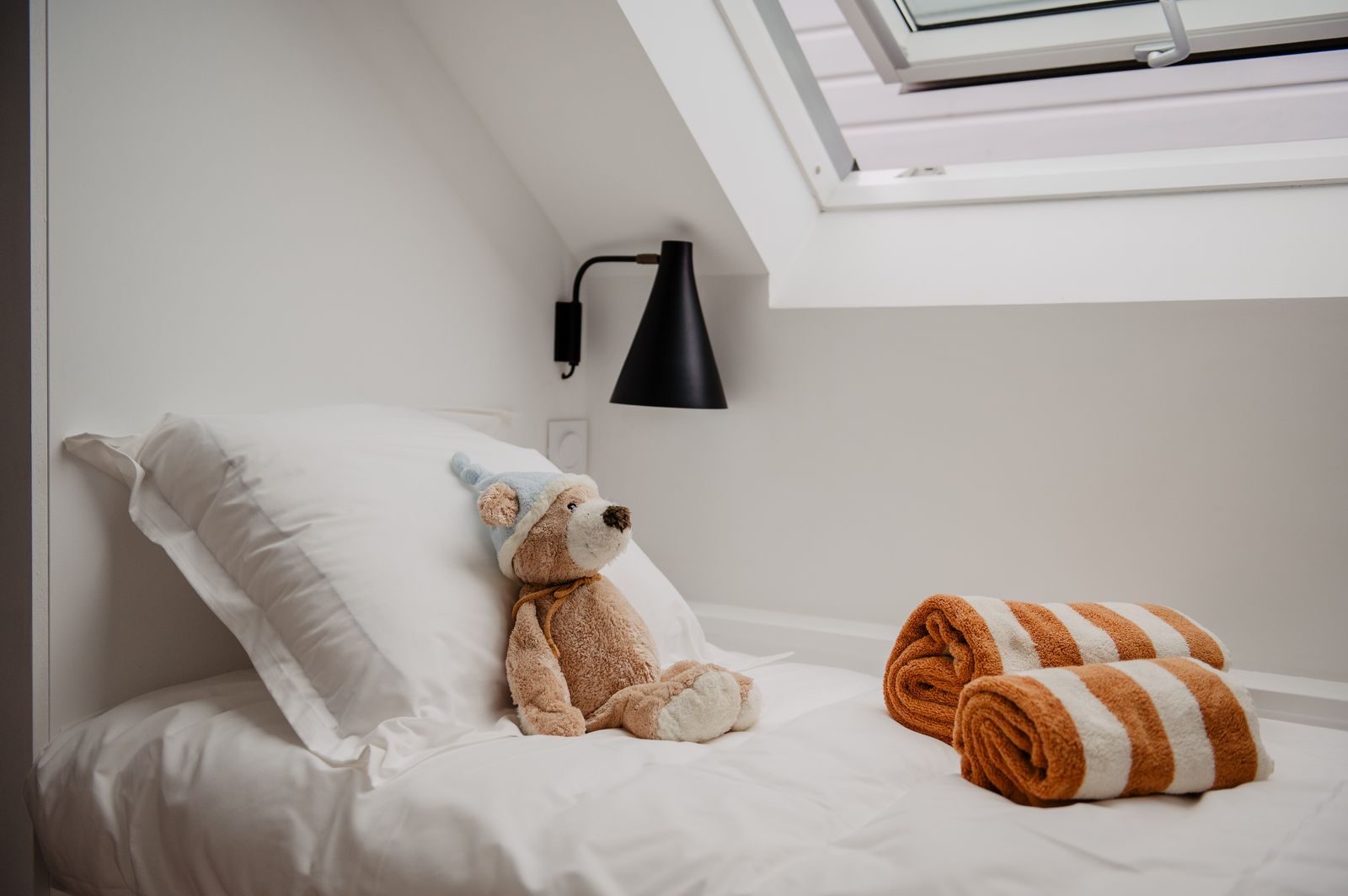 Das Zimmer von Inès und Olivia, Teddybär auf dem Bett unter dem Dachfenster