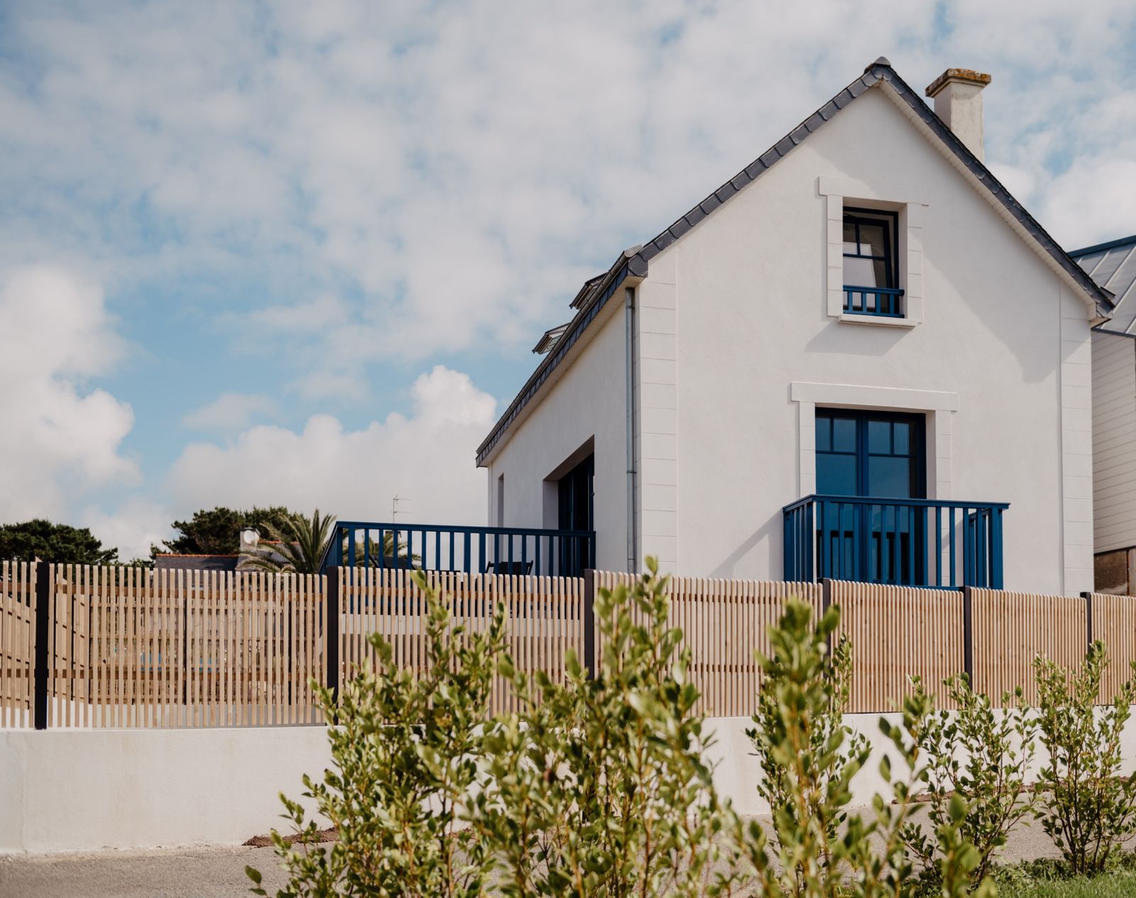 The white facade of Le Lodge de Keruster, with blue window frames and garden
